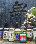 A Japanese gravestone with a calligraphic character carved into it. Many bottles and containers of alcohol are placed in front of it.