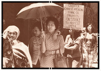 Six strikers. One holds an umbrella and drapes her arm around her friend's shoulders. Another holds a sign declaring “on strike to protest unfair labor practices.”