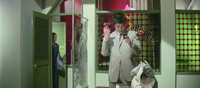 Stylish, composition depicting the nightclub office in Sasebo, with multiple, colorful door frames and latticed windows, tacky but appealing. Off-­center right is Tetsu fooling with a “Light Punch” mini-­hair dryer and cosmetic mirror, while Umetani watches from the door frame behind.