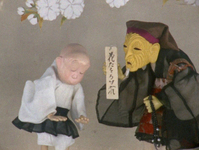 A puppet dressed like an old monk holds up a message with calligiraphic writing that warns people not to break branches. He instructs a younger monk to ensure this.