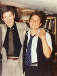 Color photo. Poore wears a sport jacket and tie; Cohen wears a vest and cardboard tie by Clsuf. Both smile toward the viewer. Poore's arm is around Cohen's shoulder. Cohen holds her hand.