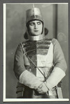 Photograph of Alisa Koonen in the armor of Joan of Arc, her heavily gloved hands clasped in front of her, her eyes to one side.