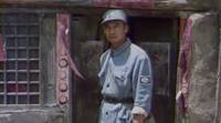 A film still of a soldier standing at a wooden doorway, with calligraphic circles painted on the frame.
