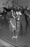 A black and white photograph of Toña La Negra at a microphone on the stage of Station XEW with Rafael Hernandez on her left and Wello Rivas on her right. A crowd is seated in the background, including a piano and string section.