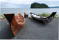 A color photograph of three decorated dugout canoes on a rocky beach.