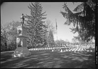 Black-­and-­white photograph of Albany Rural Cemetery Soldiers’ Lot. Standing soldier monument appears in the foreground, overlooking rows of marble soldiers’ headstones. Trees appear on either side of the lot.