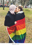 This shows two women, Kate and Sarah, kissing and wrapped in a rainbow flag in a park.