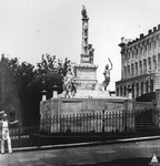 Figure 1 depicts a monument located in a fenced grassy area adjacent to the United States Capitol building, which is visible on the side of the image. The photograph is historic and shows the location around the year 1857. At the center, the Naval or Tripoli monument dominates the scene. The monument contains, from the top, an eagle and shield on a rostral column. Viewed from the side, the photograph shows three of the ship’s rams on the column; another three are not visible from this angle. Around the column and on a base below it a viewer encounters numerous relief sculptures, examples of freestanding figural statuary, and inscriptions. Important for this study are the small sculptures lining the upper edges of the column’s base that depict Orientalizing and caricaturesque faces meant to represent the peoples of the Maghreb.