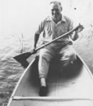 A black-and-white portrait of Leroy Grumman paddling an aluminum canoe.
