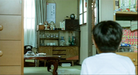 A boy looks at a frame on the wall with black calligraphy.