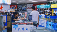 Several people browsing or working in an electronics marketplace in China—the marketplace is inside the basement of a building, with stalls selling various products.