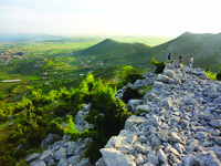 Three people stand on rocks within the Gajtan hill fort overlooking Nënshkodër, a plain in Albania.