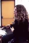 Color photo. Side view of Cohen seated, wearing a dark sweater and pants, making expressive hand gestures while talking. Long, curly hair below her shoulders.