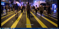 This screen shot from “One Night in Mongkok” shows a crowd in a city street at night. The sot focuses on a young man wearing a backpack who is walking away from the camera