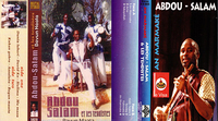 Two album covers for a music group, Abdou Salam and Les Tendistes, are displayed next to each other. The cover on the left, which has English writing on it, portrays two men standing on outdoor steps with trees in the background, with a third man sitting on a stool between them giving a thumbs-­up. The name of the group is written below the men, and the album’s track listing is written sideways on the left side of the cover. The cover on the right portrays a man, presumably the leader of the group, looking into the camera as he plays an instrument in front of a black background. The album title and track listing are written sideways in a non-­English language on the left side of the cover. A small but prominent condom advertisement sits in the middle of the cover.