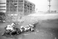 A photograph of Philippine protestors crawling on the ground, sprayed with water by water cannons, at a protest against the Marcos administration at the Welcome Rotunda, Quezon City, on September 27, 1984. Photo credit: Jacinto Tee.