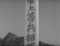 A public pillar has black calligraphy printed on it, in black and white cinematography.
