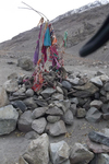 Numerous small pieces of colorful fabric are tied to four tall sticks that are set in a small wall of boulders. There are also numerous horns of different sizes from livestock. In the background is a small dirt hill. This is a Sufi religious shrine, and the pieces of fabric have been tied to the shrine as offerings by locals living in the Wakhan Valley.