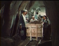 Workers move a mine cart along the tracks through a tunnel.