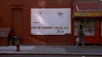 A character writest graffito on a framed area for posters: "Like an ignorant East Suit." The adjacent storefront has an awning saying "Sanchez Grocery," the name rendered cursively to evoke a signature.