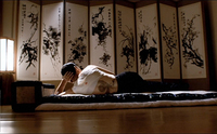 An individual lies in front a room screen divider with black calligraphy printed on it.