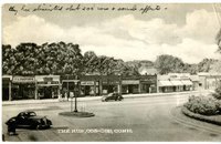 A commercial street of Cos Cob, Connecticut is depicted in this postcard. Two cars are shown against a background of shops along the town's street.