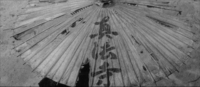 An umbrella has black calligraphy printed on it, in black and white cinematography.