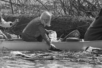 A black-and-white photograph of a Girl Scout in a canoe, picking litter out of a waterway.
