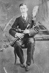 Portrait of a man sitting in a chair holding uilleann pipes (Irish bagpipes).