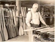 A black-and-white photograph of a figure making paddles.