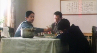 A family dining room is decorated with a work of framed calligraphy. The family eats together at a table in the middle of the frame.