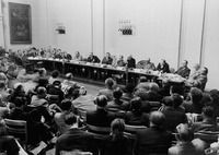 Photograph of fifteen panelists seated at a long conference table, with the audience listening attentively.