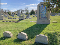 Color photograph of monuments at Druid Ridge Cemetery in Pikesville, Maryland. Family lots include large central monuments of different styles with low-­to-­the-­ground markers for individuals. Appearing in the foreground is the Hood monument, a large glass mosaic of Christ the Shepard set in granite made by the Tiffany Company, with individual granite markers graved with family names and flowers, also by the Tiffany Company, in front.