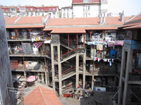 Photograph of a courtyard viewed from the top floor. It shows the external corridors, a staircase, and drying laundry hanging from lines stretched across the courtyard.