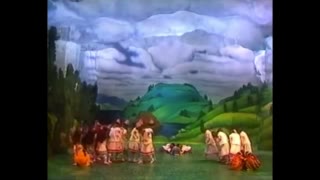 In front of a painted backdrop of hills, forest, and sky, dancers are dressed in costumes meant to invoke the indigeous.