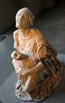 Marble statue depicting an old woman who squats on the ground and holds a lagynos flask in her lap. She is dressed in a chiton that has slipped off her shoulder, leaving her upper body uncovered, but without exposing her breast. Her heavy cloak, fallen to the ground, piles up around her.