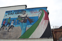 A mural painted on a building depicts a Palestinian man carrying a bleeding boy on a Gaza beach. At right is a blood-stained Palestinian flag.