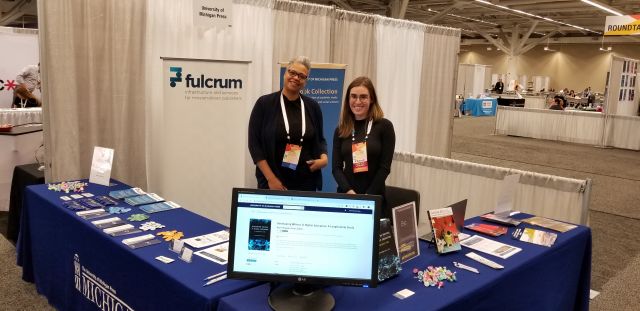 A photograph of Emma DiPasquale and Lanell White at the Fulcrum + U-M Press EBC Booth at ACRL